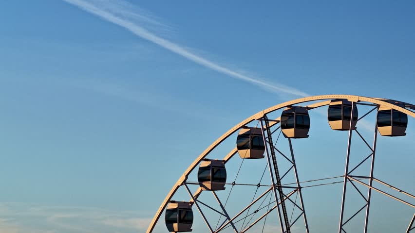 Big observation wheel with cabins turning for tourists at a fairground during a sunny day