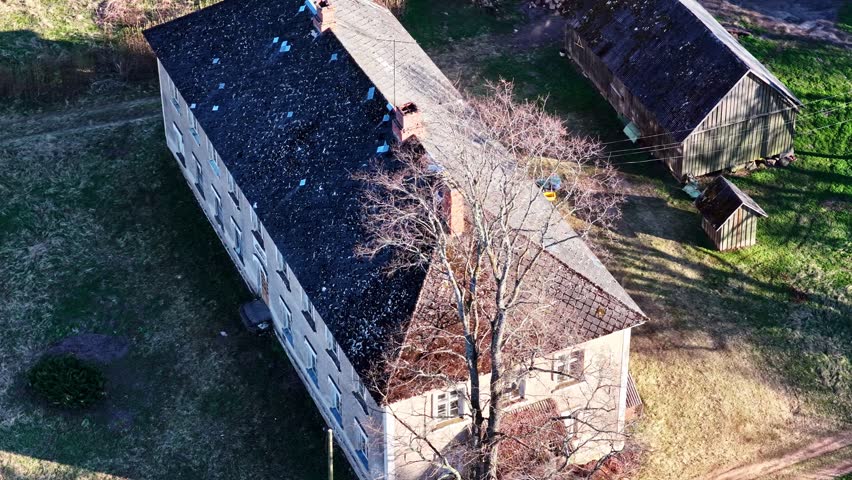 Aerial perspective of an old, abandoned apartment building surrounded by green fields and trees