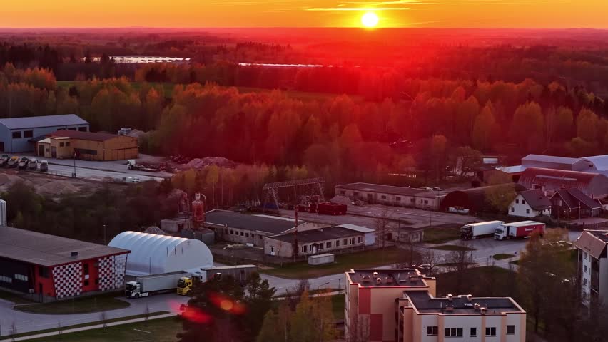 Vibrant sun setting over an industrial park and a warm-colored forest in aerial view