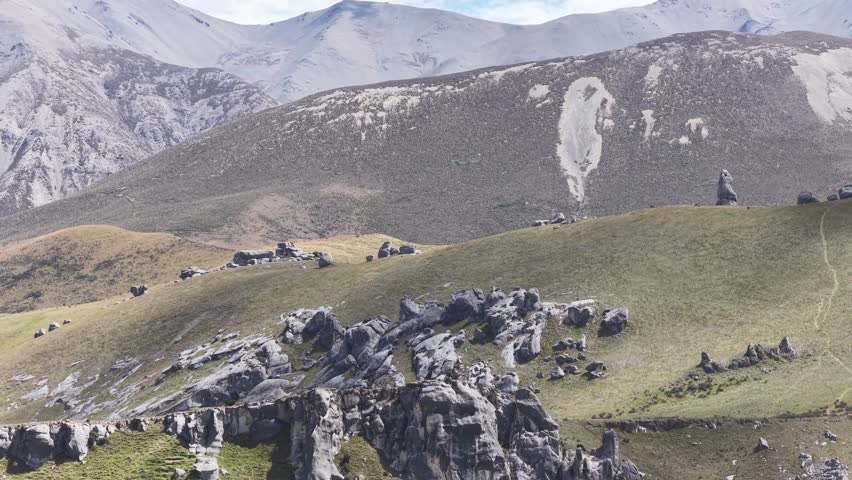 Scattered limestone boulders on green hills below snow capped mountains at Castle Hill New Zealand