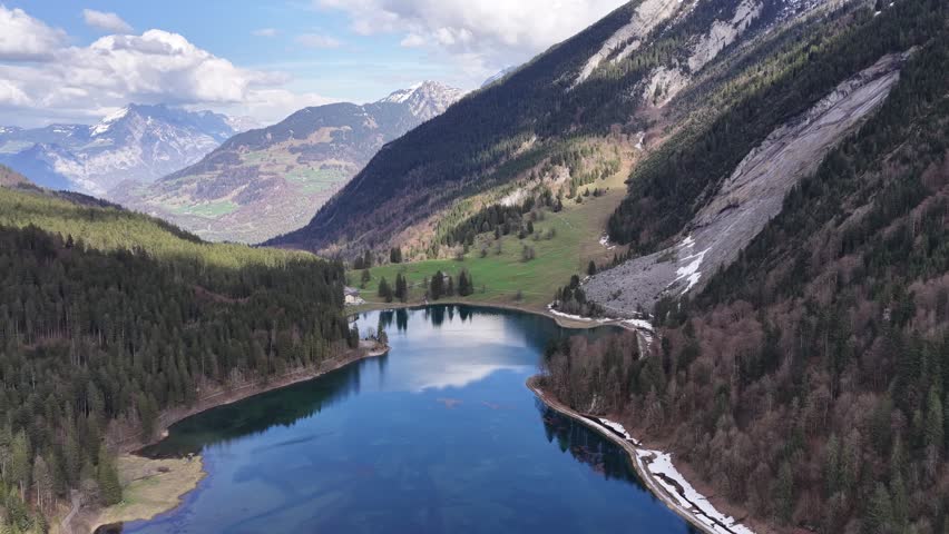 Aerial view glides over a mountain lake surrounded by forest and rocky slopes
