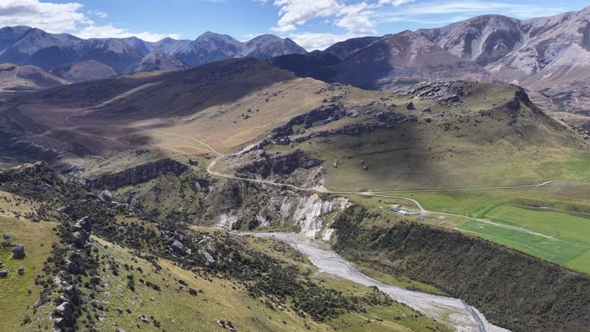 Aerial panorama of New Zealand’s South Island featuring rugged highlands, winding riverbeds, rolling grasslands, and dramatic mountain ranges under clear skies.
