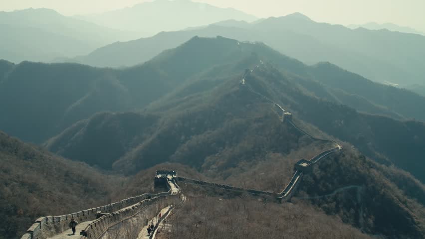 Beijing Ancient Great Wall fortification with stone watchtowers snaking along hazy mountain ridges under soft daylight