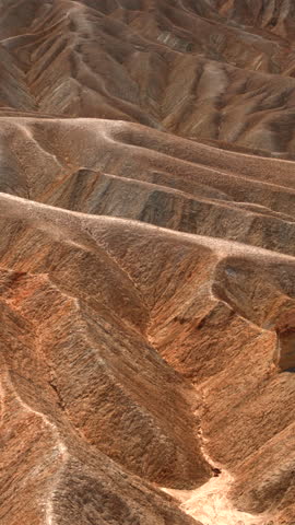 Vertical Screen: Dramatic eroded badlands at Zabriskie Point in Death Valley National Park, California. Golden sunlight illuminates intricate ridges and valleys of ancient sedimentary rock formations.