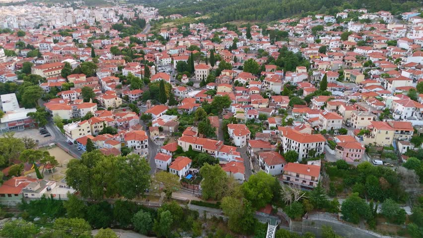 Aerial view of the historic Xanthi Old Town at sunset, Greece. Traditional Macedonian architecture and red-tiled roofs glow under the golden light of the Rhodope Mountains.