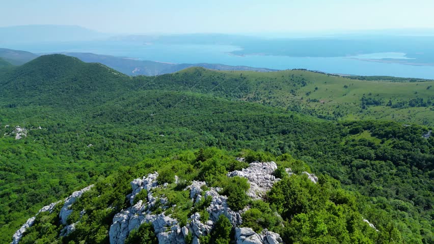 Lush green Velebit mountains meet the serene Adriatic Sea under a clear sky. An expansive aerial view of Croatia