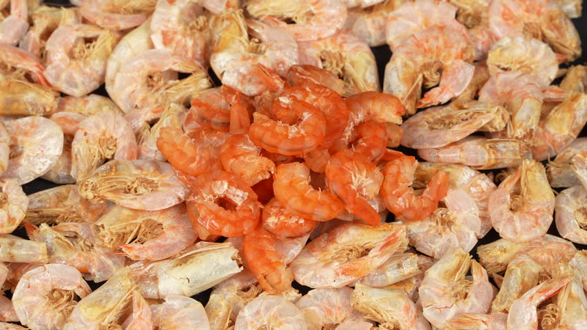 A pile of orange peeled dried shrimps on top of unpeeled prawns.