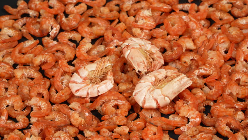 Unpeeled dried shrimps placed on top of peeled ones rotating.