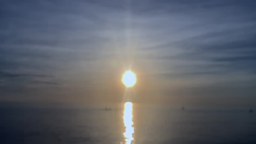 Sunrise over calm sea with distant fishing boats and paddle boarders on horizon. Peaceful morning seascape, outdoor recreation, coastal lifestyle, travel and summer vacation.