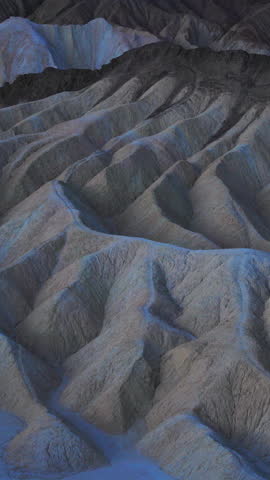 Vertical Screen: Death Valley National Park Zabriskie Point California featuring dramatic eroded mudstone badlands with deep ridges and gullies in cool blue twilight tones creating otherworldly.