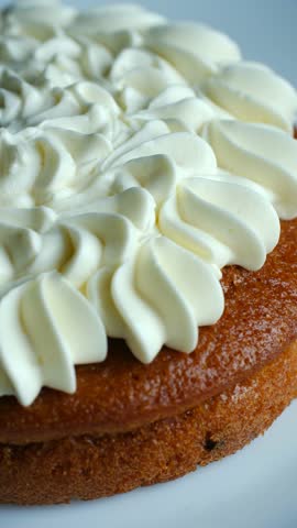 Delicious homemade carrot cake rotating on serving plate, showing golden crust white cream cheese frosting. Beautiful dessert isolated on white plate. Homemade carrot cake rotating on serving plate