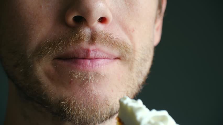 Extreme close up bearded man mouth opening wide to eat sweet, delicious carrot cake with cream cheese frosting, chewing with pleasure, enjoying dessert taste. Man eating carrot cake with cream 