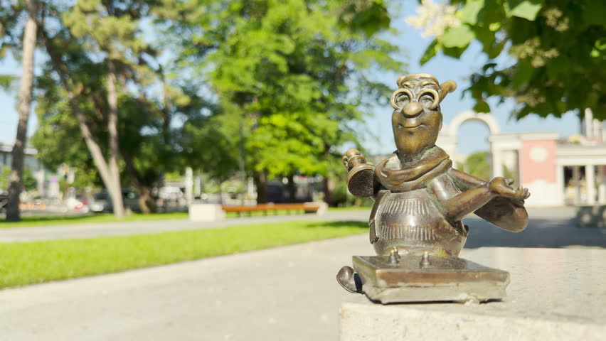 A whimsical bronze bee figurine smiles cheerfully on a stone ledge in a sunny park in Simferopol, Crimea. This cute character brings a joyful and happy feeling to the bright outdoor day.