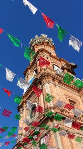 Looking up at the historic red brick tower of Our Lady of Guadalupe Church adorned with colorful flags in Puerto Vallarta Mexico