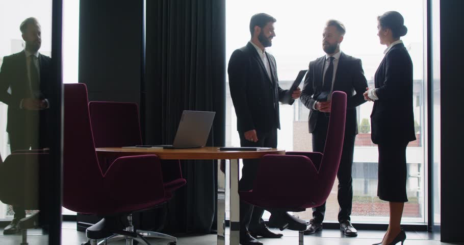 Professional business people meeting in office and working toward successful partnership. Team of three happy people standing in modern office room, exchanging handshakes and clapping hands