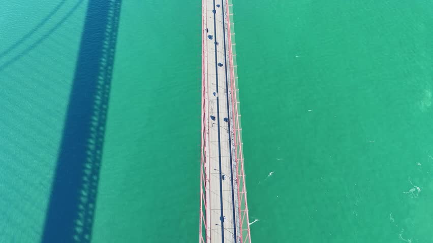 A high-angle, top-down drone shot looking directly down at the iconic red suspension bridge spanning the vibrant turquoise waters of the San Francisco Bay