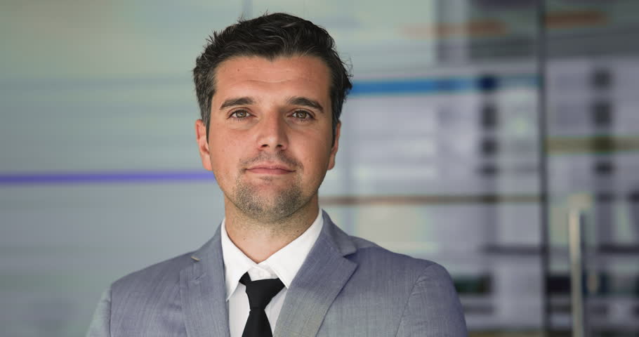 Positive confident young Latin businessman in formal suit standing in office for head shot, getting happy, smiling. Professional portrait of successful business leader man, CEO, executive, manager
