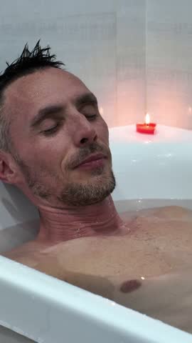 A happy man lies in the bathtub and is completely immersed in water, enjoying the water treatments
