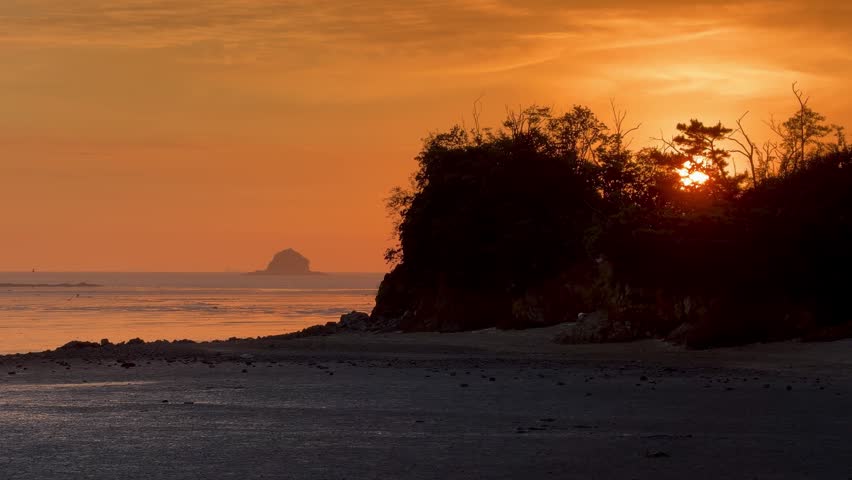 Dramatic sunset over ocean beach with orange sky, dark coast, and distant island