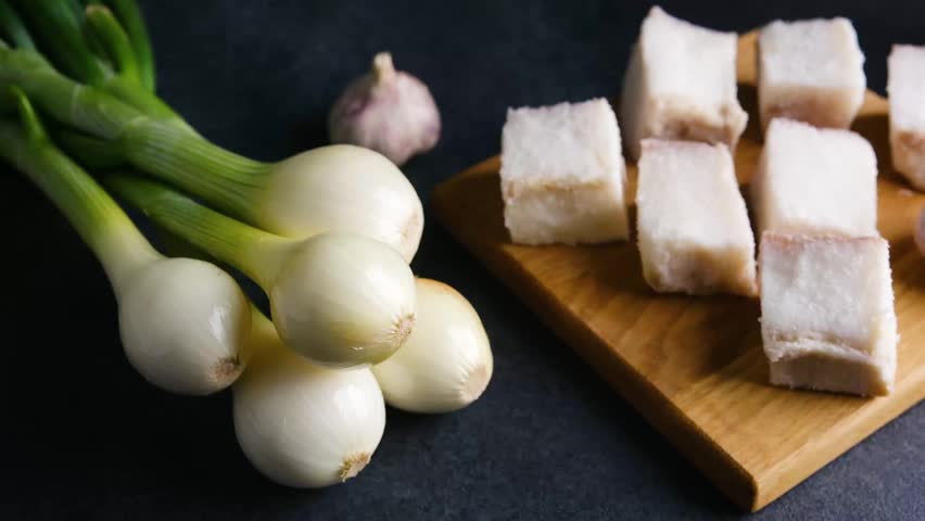 Raw bacon pieces and spring onions on a wooden board