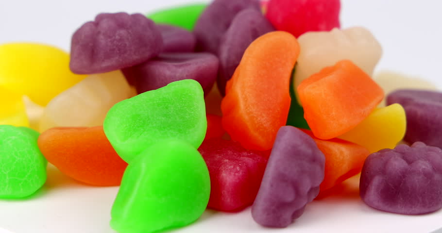 Close up spinning view of colorful fruit shaped candy candies on a round ceramic plate device layout over bright studio background