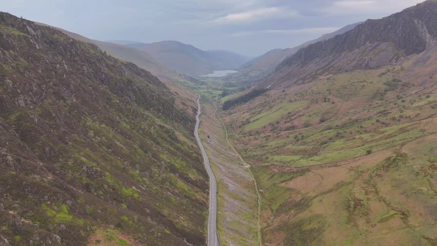 An aerial landscape view of a road in green mountains under cloudy sky in Wales