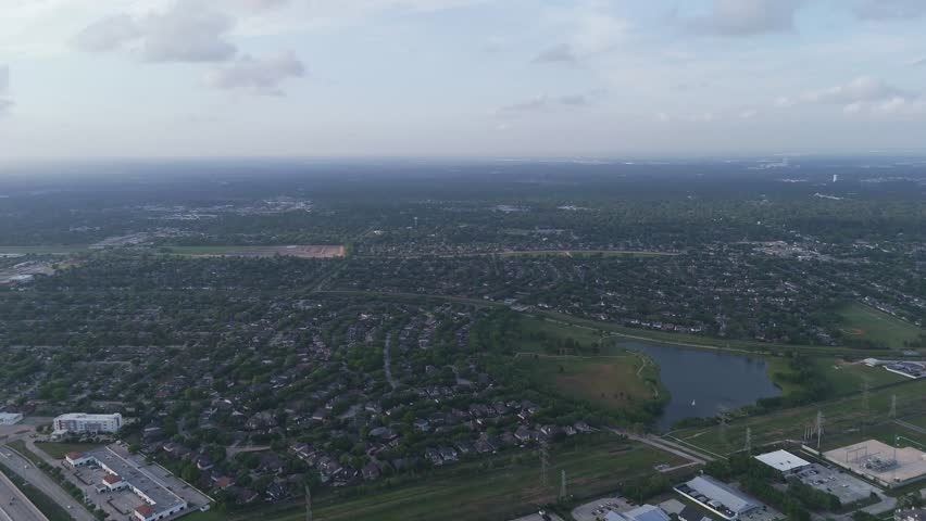 An aerial shot looking over a residential area featuring houses, a small lake, and power lines under a cloudy sky, Houston, Texas