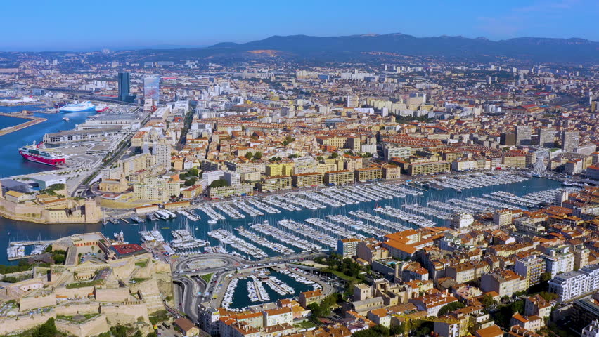 Aerial drone view of the Vieux Port of Marseille with moored yachts, Fort Saint-Jean, the harbor ferris wheel, and CMA CGM Tower in Marseille, France, daytime.