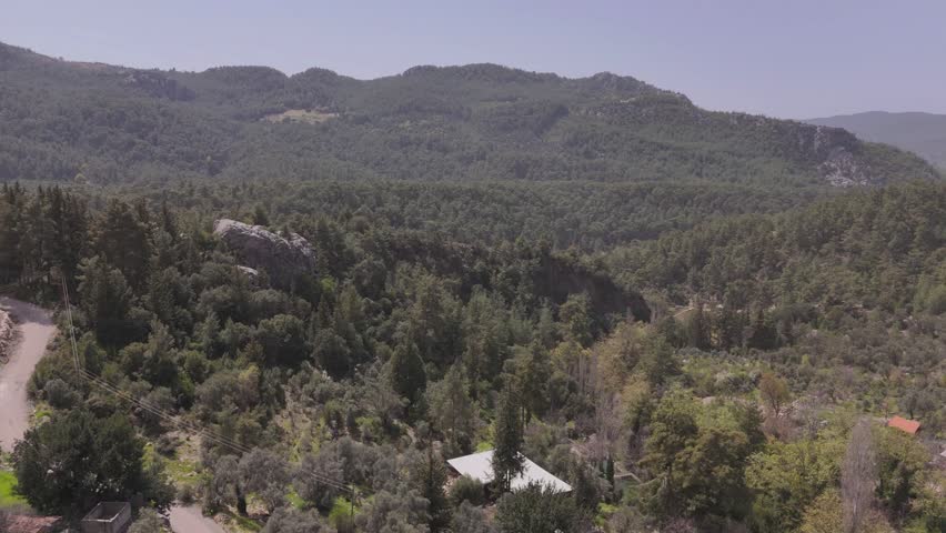 A drone view of forested mountainous countryside landscape with scattered cottages on a sunny day with blue sky in Hasdumen, Antalya, Turkey