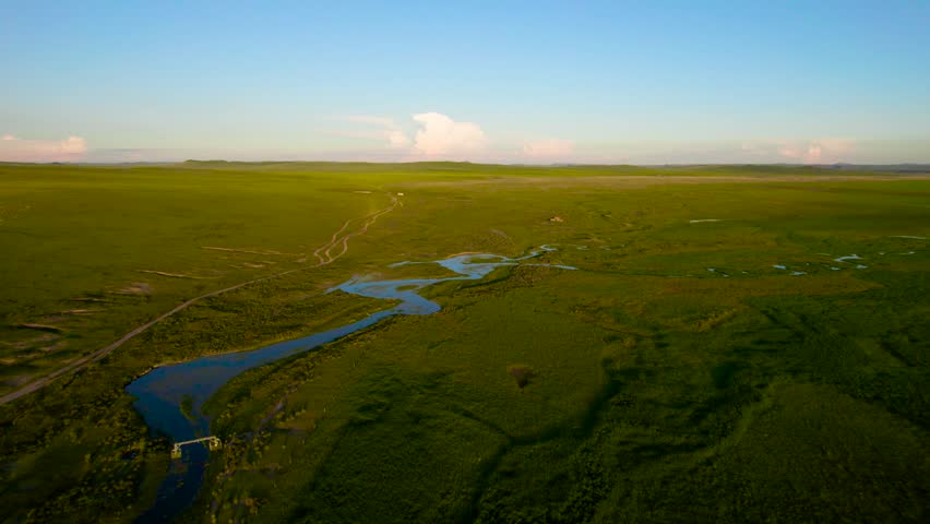 Drone overlooks boundless green grassland Inner Mongolia China,multiple branched rivers interweave into river network,gentle mountain ranges stand far away under sky