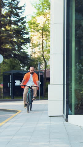 Handsome bearded smiling man riding bicycle at downtown district. Professional young male going to work and typing by phone while sitting on the bench with bicycle in background.