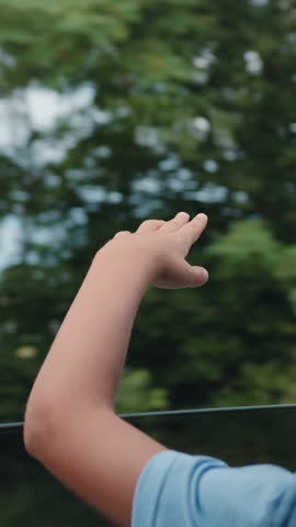 Back view. Happy child stretched out his hand from the car window. Boy waving hands gesturing out of the car window during a trip with his family. Slow motion.