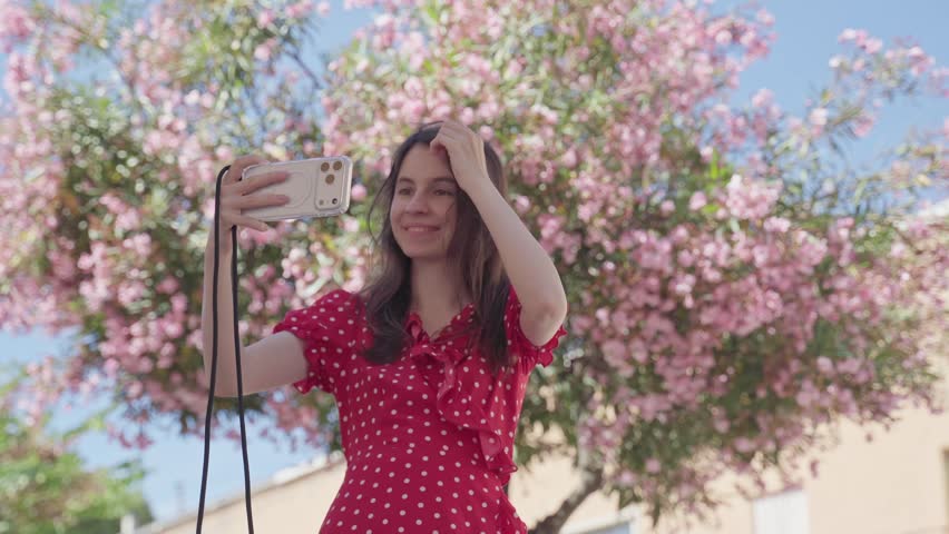 Young Woman Taking Selfie And Showing Peace Sign Under Pink Flowers