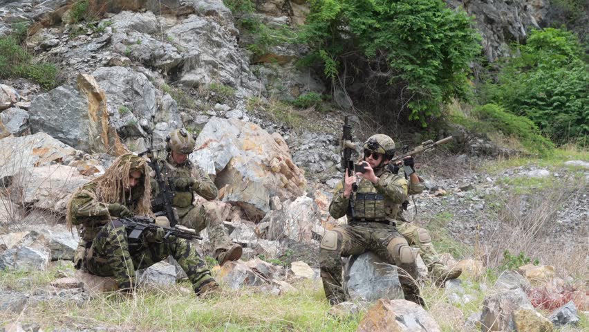group of soldiers in military uniforms, holding rifles and practicing combat against the enemy, stand at rest during a training exercise on the battlefield.
