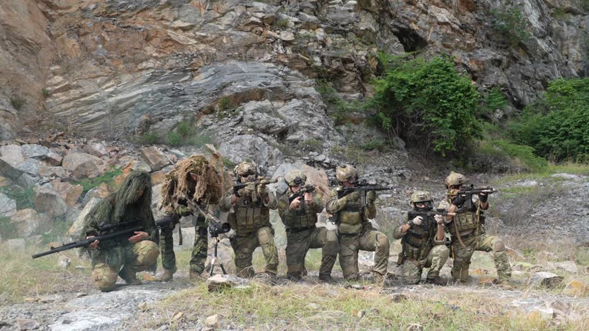 A group of soldiers in military uniforms stand holding BB guns, keeping a watchful eye on enemies during a patrol while exercising their military training, in order to play the game.