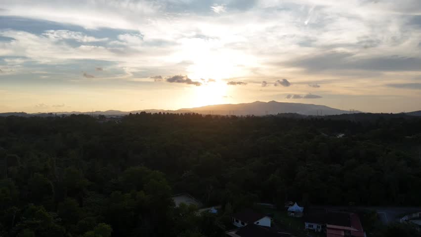 Aerial drone footage of a golden sunset over tropical forest and distant hills in Johor Bahru, Malaysia. Vertical 4K cinematic landscape featuring warm evening light, dramatic clouds and peaceful natural scenery.