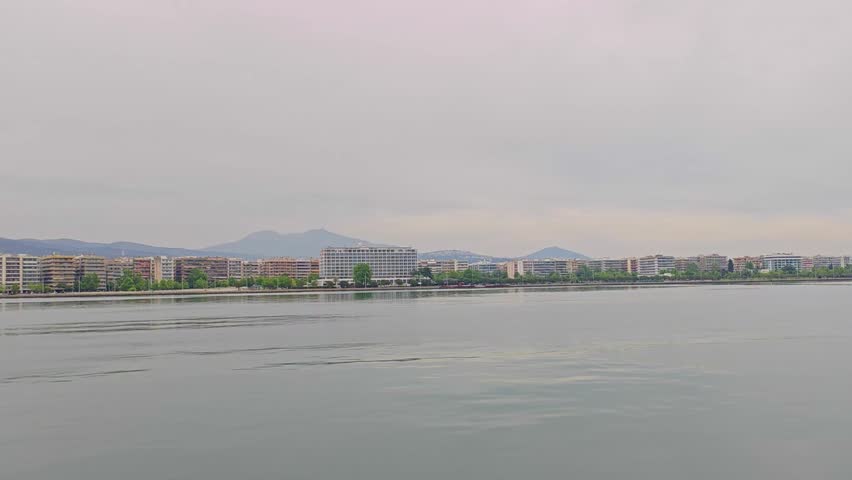 View from boat on water and buildings near water in Thessaloniki, Greece. Side view of City on coast of Thermaic Gulf 