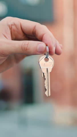Close-up hand holding key from a new house outdoor. Slow motion.