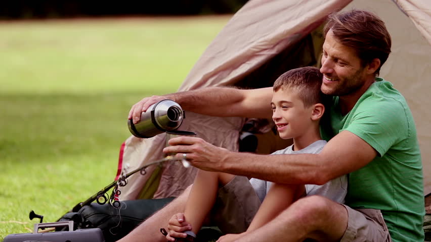 Father pouring tea in a cup in front of his tent