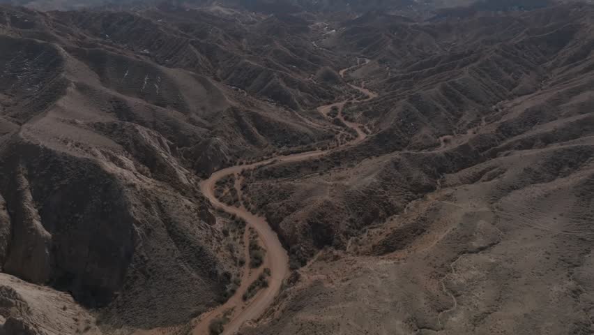 Drone footage of rugged Skazka Canyon with eroded desert hills and a winding unpaved road through the valley, Issyk-Kul Region, Kyrgyzstan
