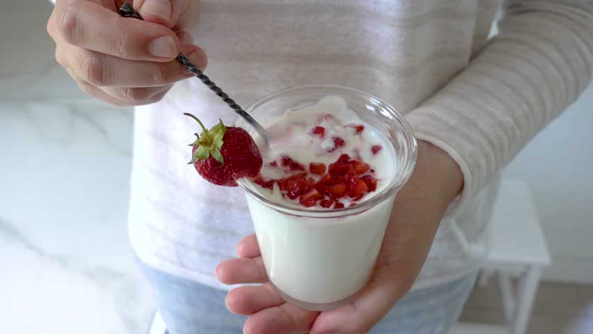Hands stirring strawberry yogurt in a glass with a spoon. Symbolizes probiotics, healthy eating, and the nutritional value of dairy products. Top view. Ideal for wellness, food, and lifestyle content