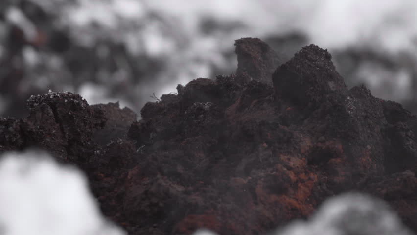 Dark charred rock formations with rough porous texture and soft gray haze in close macro view, creating gritty abstract industrial atmosphere with muted black, rust, and charcoal tones