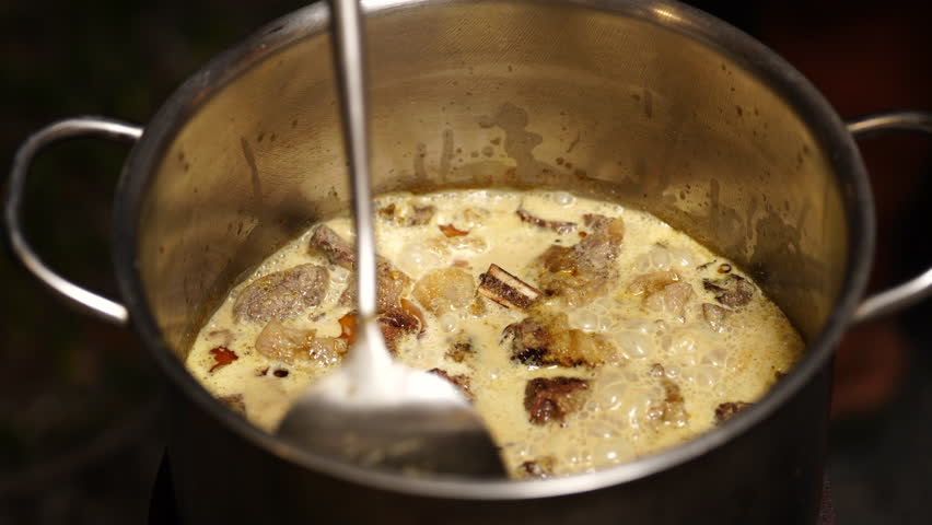Traditional thai food, Meat pot stew cooking spoon creamy broth beef kitchen metal food preparation with tender chunks in savory dairy base, ladle handle, steam, rustic homemade dinner closeup