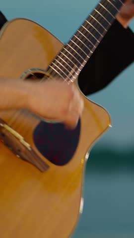 Close-up of musician strumming acoustic guitar against soft blue background