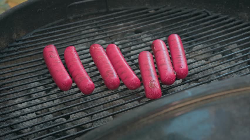 Bright red hot dogs cooking on charcoal grill