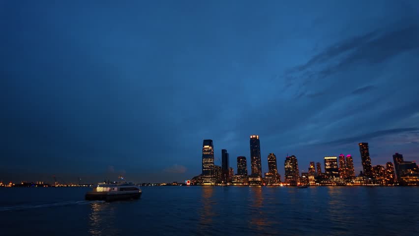 Twilight skyline and passenger ferry, Jersey City, New Jersey. A small boat moves across the Hudson River while office lights shimmer on the water.
