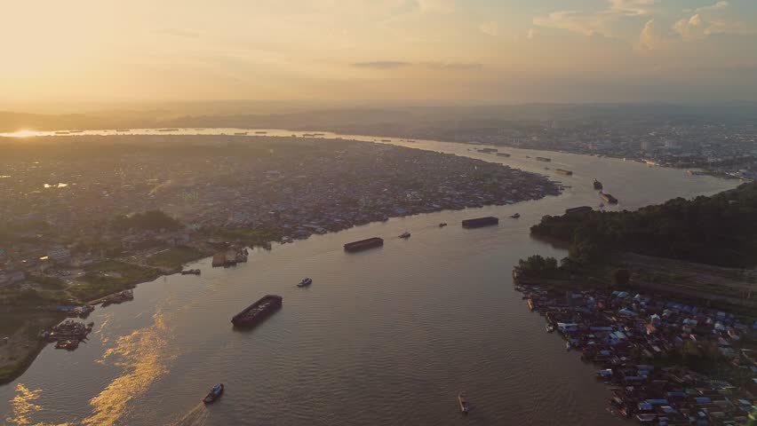Aerial view of Mahakam River flowing through the city with barges and boats on the water at sunset in Samarinda, East Kalimantan, Indonesia.
