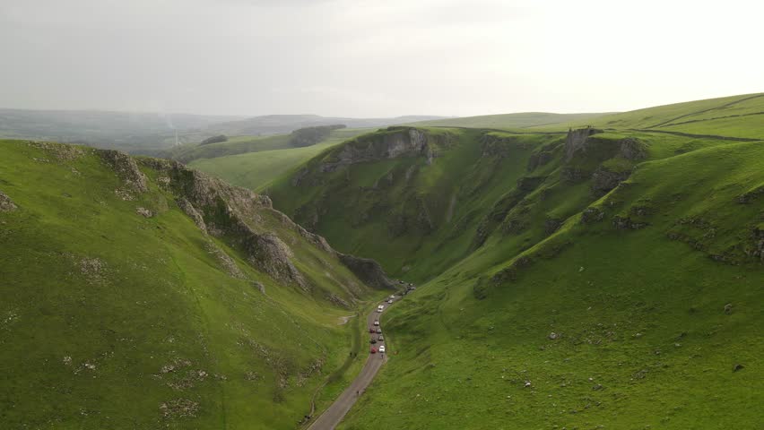 Aerial view of the winding road through the limestone gorge of Winnats Pass with green hills and cars in Hope Valley, England, United Kingdom.