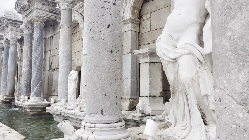 Close pan shot of intricately carved marble statues and structural pillars inside the Antonine Nymphaeum fountain house in Sagalassos, Turkey.