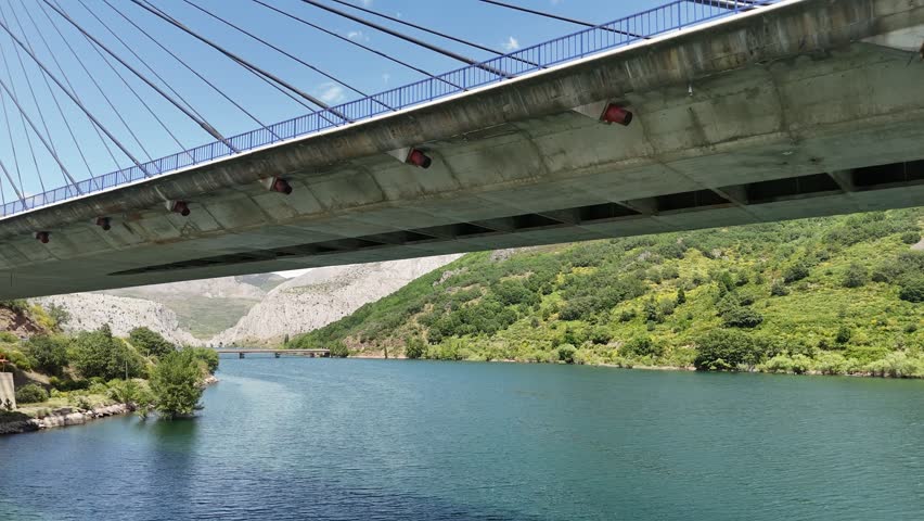 View under a large concrete bridge crossing a blue reservoir between green mountains